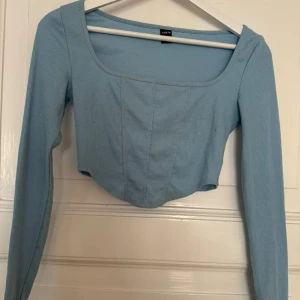 Ljusblå croppad topp  - Säljer en ljusblå croppad topp från SHEIN med lång ärm och fyrkantig urringning. Toppen är ribbad och har en figurnära passform som framhäver siluetten. Perfekt att matcha med höga jeans eller kjol för en trendig look.