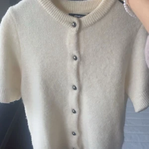 Vit kofta från Gina Tricot med kort ärm - Superfin vit kofta från Gina Tricot med korta ärmar och rund hals. Koftan är stickad i mjukt material och har snygga silvriga knappar framtill. Använd några gånger 