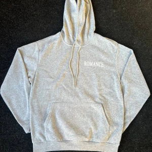 Grå Romance hoodie - 🩶 Färgglad grå hoodie med vit text “ROMANCE” framtill och stort tryck på ryggen med duvor. ✔️ Stor ficka framtill (känguruficka) ✔️ Dragsko i huvan ✔️ Mjuk och bekväm passform ✔️ Perfekt vardagströja med lite streetwear-känsla  📏 Storlek: M ✨ Skick: Väldigt bra, ny