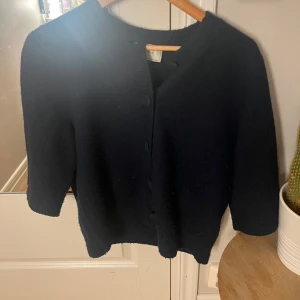 Mörkblå stickad kofta med knappar - mörkblå stickad kofta från Neo Noir med tygklädda knappar framtill. Koftan har trekvartsärm och ribbade detaljer. Används typ 3 gånger, känner inte att de är min stil. Storlek S. Köpt för 700kr.