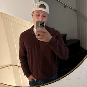 Vinröd half zip från Polo Ralph Lauren - Vinröd långärmad tröja från Polo Ralph Lauren i mjuk pima bomull. Klassisk half zip-dragkedja och broderad logga på bröstet. Perfekt för lager-på-lager och snygg till jeans eller chinos.