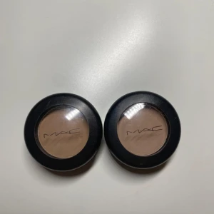 MAC Omega Matte Ögonskugga x2 - Två stycken MAC Omega Matte ögonskuggor i en snygg, kall beige-brun nyans. Kommer i klassiska svarta runda MAC-förpackningar med genomskinligt lock. Perfekt för naturliga looks eller som skugga till brynen.