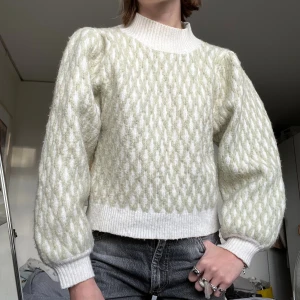 Vit och ljusgrön stickad tröja från ASOS - Supermysig stickad tröja från ASOS i vit och ljusgrön färg med mönstrad struktur. Tröjan har puffiga långärmar, ribbade muddar och hög ribbad krage. Perfekt för dig som gillar en chill och trendig look med lite volym i ärmarna.