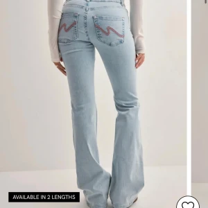 Nelly Jeans - Snygga ljusblå jeans med bootcut passform och broderade detaljer i rosa på bakfickorna. Jeansen har låg midja och är tillverkade i klassiskt denimtyg. Perfekta för en trendig och avslappnad look.