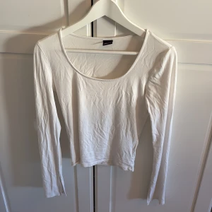 Vit långärmad topp från Gina Tricot - En basic vit långärmad topp från Gina Tricot i mjuk och stretchig bomull. Modellen är enkel med rund halsringning och smal passform, perfekt att styla till jeans eller kjol. Superenkel att matcha och ett måste i garderoben.