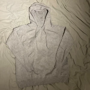 Ljusgrå hoodie med huva och snörning - En stilren ljusgrå hoodie med huva och snörning. Tröjan har långa ärmar och ribbade muddar vid ärmslut och nederkant. Perfekt för en chill och avslappnad look. Materialet känns mjukt och skönt mot huden.