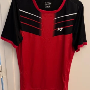 Forza Check röd tränings t-shirt - Forza Check T-shirt - ett bra alternativ på din nästa tränings t-shirt om du önskar hög komfort och ventilation. Den ger dig fri rörlighet på banan tack vare dess kvalitetsmaterial av återvunnen polyester. Materialet är töjbart och ger dig en bra passform och komfort.  T-shirten har DryForze teknik som garanterar ventilation och svettabsorbering. Den kommer här i en cool design i rött med svarta detaljer.  Nypris 599 kr