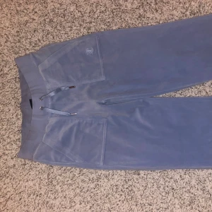 Blå juicybyxor - Snygga ljusblp juicy byxor med bred resår i midjan och snörning framtill. Byxorna har stora fickor fram och en bakficka med knapp. Mjukt material som känns skönt mot huden och passar perfekt för chill dagar. Nästan helt oanvänd!!!!