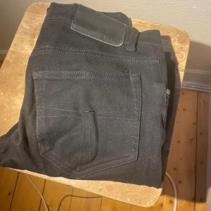 Svarta jeans med raka ben från Tiger of Sweden - Snygga svarta jeans med klassiska bakfickor och raka ben. Jeansen har en enkel design med tydliga sömmar och är tillverkade i ett slitstarkt denimtyg. Perfekt för dig som gillar en clean och stilren look.