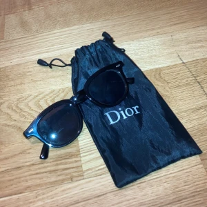 Svarta Dior solglasögon - Snygga svarta solglasögon från Dior med klassisk rundad wayfarer-form. Kommer med original svart fodral med Dior-logga. Glasögonen har en stilren och tidlös look som passar perfekt till alla outfits.