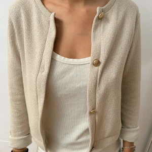 Beige kofta med guldfärgade knappar - Snygg beige kofta med guldfärgade knappar framtill. Materialet är stickat och ger en mjuk och chill känsla, perfekt för att lyfta din outfit💕