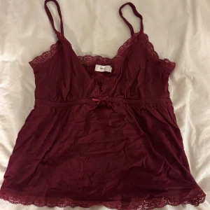 Vinröd spetskantad linnetopp från Nelly - Supersöt vinröd linnetopp från Nelly med tunna axelband och v-ringning. Toppen har fina spetsdetaljer längs urringning och nederkant samt en liten rosett framtill. Tillverkad i mjuk bomullsmix, perfekt för en chill och romantisk look.