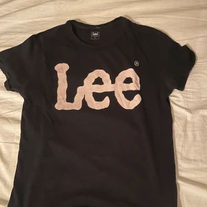 Svart Lee t-shirt - Svart t-shirt från Lee med stor vit logga framtill. Klassisk rund hals och korta ärmar. Skön passform och tillverkad i mjuk bomull, perfekt för en avslappnad stil.