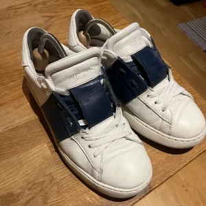 Valentino Garavani Open sneakers vit/blå - Tja, jag säljer ett par valentino opens. som ni ser är dem i bra skick eftersom dem har varit inne på fixning och lagning. det man ser det är mest vid häl stödet där en grå extra platta har behövts läggas till. man ser inte det från utsidan så spelar ingen roll. sulan är ganska använd men inte för mycket så att det inte finns något fäste. Har du någon fundering tveka inte att kontakta.