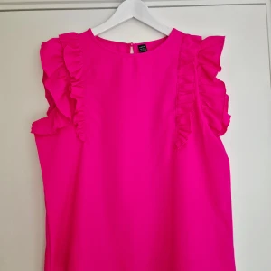 Rosa volangtopp från SHEIN - Säljer en rosa ärmlös topp från SHEIN i storlek L. Toppen har volangdetaljer längs axlarna. Tillverkad i 100% polyester. 