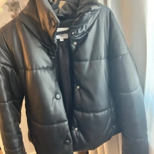 Svart pufferjacka i skinnimitation NA-KD - Säljer en svart pufferjacka från NA-KD i skinnimitation. Jackan är väldigt tjock vilket gör att den passar perfekt som vinterjacka! Den är super snygg och knappt använd och därav inga defekter alls🩷