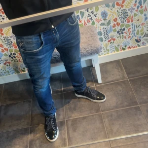 Blå Replay Anbass slim fit jeans - Säljer ett par snygga blå jeans från Replay, modell Anbass med slim fit. Jeansen har klassisk femficksdesign, normal midja och tydliga Replay-detaljer på fickan. Perfekta för dig som gillar en smalare passform och stilren look.