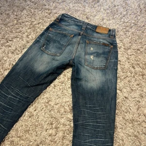 Nudie jeans Grim trim med slitningar - Nudie jeans modell Grim Trim i storlek 29/32 sjuk wash med sköna slitningar. Mycket bra skick utan defekter.Ny pris runt 1599kr. Postas antingen samma dag eller dagen efter(ANVÄND INSTABOX) Skriv gärna innan du köper 
