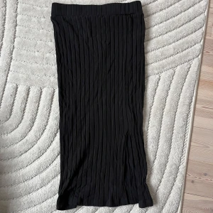 Svart långkjol med ribbad struktur - En svart långkjol med snygg ribbad struktur och rak passform. Kjolen har en enkel midjeresår och har en slits 