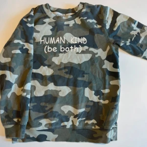 Camo sweatshirt från Ica I Love Eco - Grön, grå och beige camouflagemönstrad sweatshirt med trycket 'HUMAN. KIND (be both)' på bröstet. Tröjan har rund hals, långa ärmar och är gjord i ekologisk bomull. Perfekt för dig som gillar streetstyle och vill sticka ut lite extra.