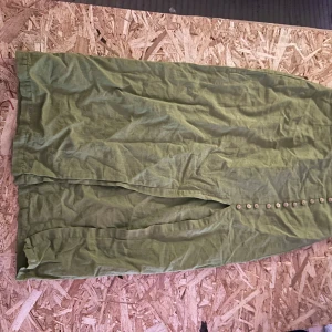 Grön midkiol med knappar från Zara - Snygg grön midkiol från Zara med raka linjer och dekorativa knappar längs framsidan. Kjolen har dragkedja i sidan och är tillverkad i ett lätt och luftigt linnematerial. 