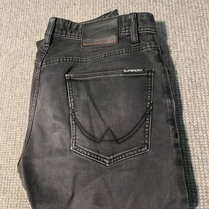 Svarta jeans från Superdry Wilson Jersey - Säljer ett par svarta Superdry Wilson Jersey jeans med snygg tvättad look och klassiska fem fickor. Jeansen har en rak passform och är tillverkade i mjukt denimtyg. Märkesdetaljer på bakfickan och vid linningen ger extra stilpoäng. Pris kan diskuteras, vid eventuella frågor är det bara att höra av sig.