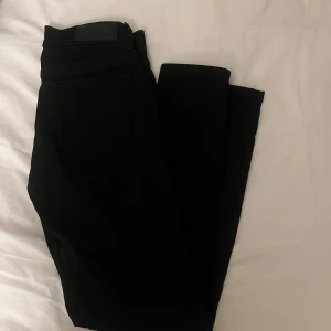 Svarta jeansbyxor med raka ben - Säljer ett par svarta jeansbyxor med klassisk femficksdesign och raka ben. Byxorna har silverfärgade nitar och knapp framtill. Perfekta för dig som gillar en stilren och enkel look. Passar till det mesta och är lätta att matcha. Aldrig använda och i storlek S.