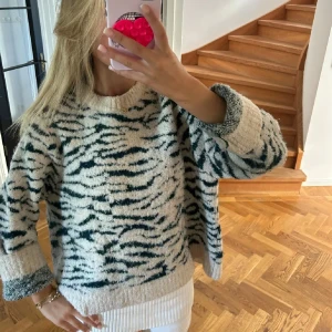 Beige och mörkgrön zebra-mönstrad tröja - Säljer en mysig beige tröja med mörkgröna zebraränder. Tröjan har en loose passform, rund hals och långa ärmar. Materialet är stickat och känns fluffigt och skönt mot huden. Perfekt för dig som gillar djurmönster och vill ha en chill vibe.