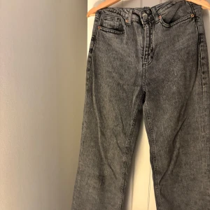Grå tvättade vida jeans  - Säljer ett par grå tvättade jeans med vida ben och klassisk femficksdesign. Jeansen har hög midja och snygga detaljer med kopparfärgade nitar. Perfekta för en avslappnad och trendig look.