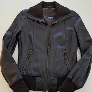 Svart skinnjacka från Goldstein, strl 38 - Snygg svart skinnjacka från Goldstein i äkta , väldigt mjukt läder. Jackan har ribbade muddar och krage, två fickor med dragkedja och en klassisk bomberjacke-look. Jackan är väldigt lite använd, som ny. Perfekt för dig som gillar stilrena och tidlösa plagg med edge.