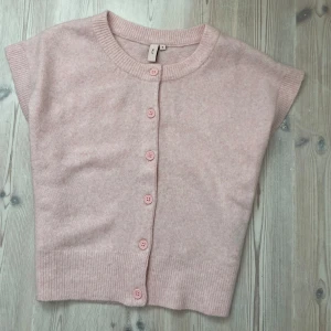 Ljusrosa kofta från Nelly i stickat - Supersöt ljusrosa kofta från Nelly i stickat material. Kortärmad modell med rund halsringning och matchande rosa knappar framtill. Perfekt att slänga över en topp för en chill look. Ribbstickade detaljer vid hals, ärmslut och nederkant.