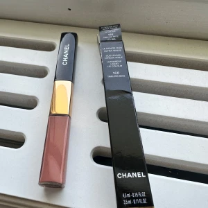 Chanel Le Rouge Duo 166 Timeless Beige läppstift  - Chanel Le Rouge Duo Ultra Tenue i färgen 166 Timeless Beige. Flytande läppfärg med två ändar – en beige-rosa nyans och en transparent gloss. Lyxig förpackning med svart och guld detaljer. Perfekt för dig som vill ha hållbara och snygga läppar.