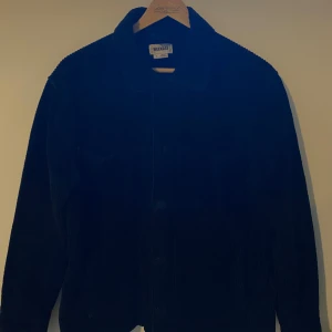 Svart manchester overshirt från Weekday - Svart overshirt från Weekday i mjuk manchester. Klassisk krage, knäppning framtill och långa ärmar. Perfekt att slänga över en hoodie eller t-shirt för en chill look. Enkel och stilren design som funkar till det mesta.