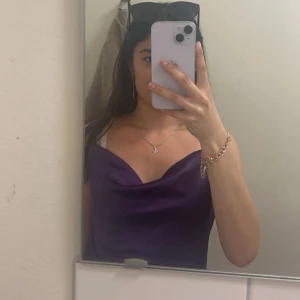 Lila satin klänning med cowlneck - Säljer ett  lila linne i satin med snygg cowlneck-ringning och smala axelband. Perfekt för dig som vill sticka ut med en trendig och elegant look. Linnet har en figurnära passform och är ärmlös.