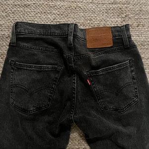 Levi's 502 svarta jeans W29 L30 - Svarta Levi's Premium 502 jeans med klassisk femficksdesign och raka ben. Jeansen har en snygg mörk tvätt, normal passform och är tillverkade i slitstarkt jeanstyg. Perfekta för dig som gillar en stilren look med lite edge.