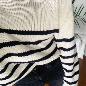 Randig stickad tröja i vitt och svart - Säljer en snygg stickad tröja med breda svarta ränder på vit botten. Tröjan har lång ärm och en avslappnad passform, perfekt att slänga på sig till jeans. Klassisk och tidlös design som funkar året runt. Passar som en s-m