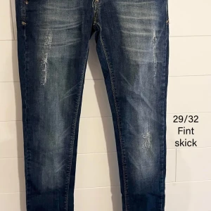 Mörkblå jeansbyxor med slitningar - Säljer ett par mörkblå jeansbyxor med snygga slitningar och dragkedja. Jeansen har klassisk femficksdesign och smal passform. Perfekta för dig som gillar en lite tuffare look. Materialet är jeans och färgen har en schysst tvättad effekt.