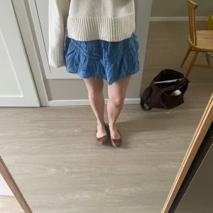 Blå volangkjol med spetsdetaljer - Supersöt blå kortkjol med volanger och dekorativa spetsdetaljer. Kjolen har en luftig och lätt känsla, perfekt för varmare dagar. Den har en avslappnad passform och är tillverkad i ett mjukt tyg som ger en skön vibe.