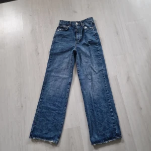 Blå wide jeans från Gina Tricot - Säljer ett par blå jeans från Gina Tricot, modell 'perfect jeans'. De har hög midja, raka och vida ben samt råa, fransiga benslut. Klassisk femficksmodell i kraftig denim med snygg tvätt. Perfekta för en avslappnad och trendig look.