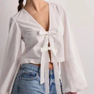 Vit blus - Säljer en vit omlottopp med långa puffärmar och två knytband framtill. Toppen har v-ringning och croppad passform, perfekt att styla med jeans eller kjol. Tillverkad i lätt bomullstyg för en luftig känsla. Lite använd. ORDPRIS: ca 400kr