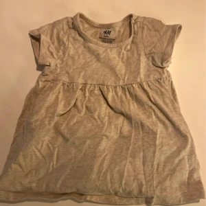 Beige kort klänning från H&M - Supersöt beige kort klänning från H&M i mjuk ekologisk bomull. Modellen har korta ärmar, rund halsringning och lätt rynkad kjoldel för en gullig look. Perfekt för varma dagar och enkel att matcha med andra plagg.