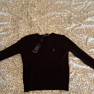 Svart stickad tröja från Polo Ralph Lauren - Svart stickad tröja från Polo Ralph Lauren med röd logga. Aldrig använd och säljer på grund av att den är för liten 