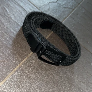 Svart bälte  - Snyggt svart flätat bälte med klassiskt svart metallspänne och detaljer i skinn. Bältet är i bra skick.