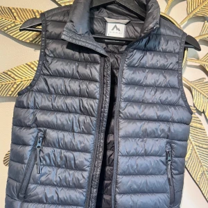 Svart dunväst från McKinley 146/152 - Obefintligt använd! Max en gång. Snygg svart dunväst från McKinley med quiltad design och hög krage. Västen har två praktiska fickor med dragkedja och diskret McKinley-logga på axelbanden. Perfekt att slänga över en hoodie för extra värme under kyliga dagar.