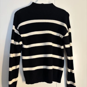 Svartvit randig stickad tröja - Snygg svart stickad tröja med vita horisontella ränder och ribbad struktur från Vila. Tröjan har lång ärm och en något högre halsringning. 