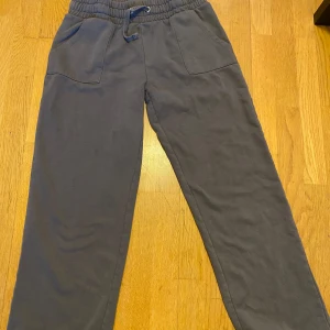 Grå mjukisbyxor från 157, storlek L - Mörkgrå mjukisbyxor från 157 i storlek L. Byxorna har resår och snörning i midjan, två stora fickor fram och en bakficka. Tillverkade i mjukt bomullsmaterial, perfekta för chill dagar eller träning.