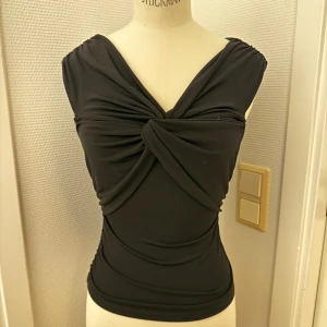 Svart omlottopp med twistad front XS - Snygg svart topp från BIK BOK med omlottkänsla och twistad detalj framtill. Toppen är ärmlös med breda axelband och har en smickrande, figurnära passform. Stretchigt material som sitter bekvämt. XS. Hämtas i Hägersten om du vill slippa frakt. Var även uppmärksam på när Plick erbjuder fraktfritt ibland på dyrare plagg. Följ mig gärna. Har mycket att lägga ut i olika storlekar! 