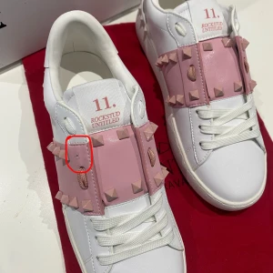 Valentino Rockstud Untitled sneakers rosa/vit - Snygga Valentino Rockstud Untitled sneakers i vitt skinn med breda rosa band och ikoniska pyramidnitar. Skorna har rund tå, platt sula och vita snören. Märkeslogga på plös och sula, samt coola detaljer runt hela skon. Perfekta för dig som vill sticka ut med lyxig streetstyle.