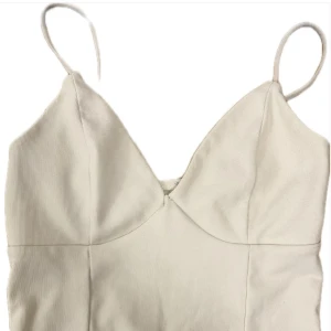 Vit ribbad topp med smala band att knyta  - Säljer en stilren vit linnetopp med smala axelband och v-ringad front. Toppen är ribbad och har knytning i ryggen för en snygg passform. Perfekt att matcha med jeans eller kjol för en fräsch look.