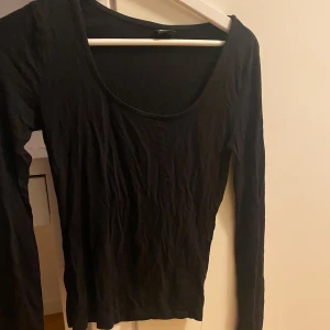 Svart långärmad topp Gina Tricot - En svart långärmad topp från Gina Tricot med rundad, djup urringning. Modellen är tight och figurnära, tillverkad i mjuk bomullsmix. Perfekt att styla med jeans eller kjol för en clean look.